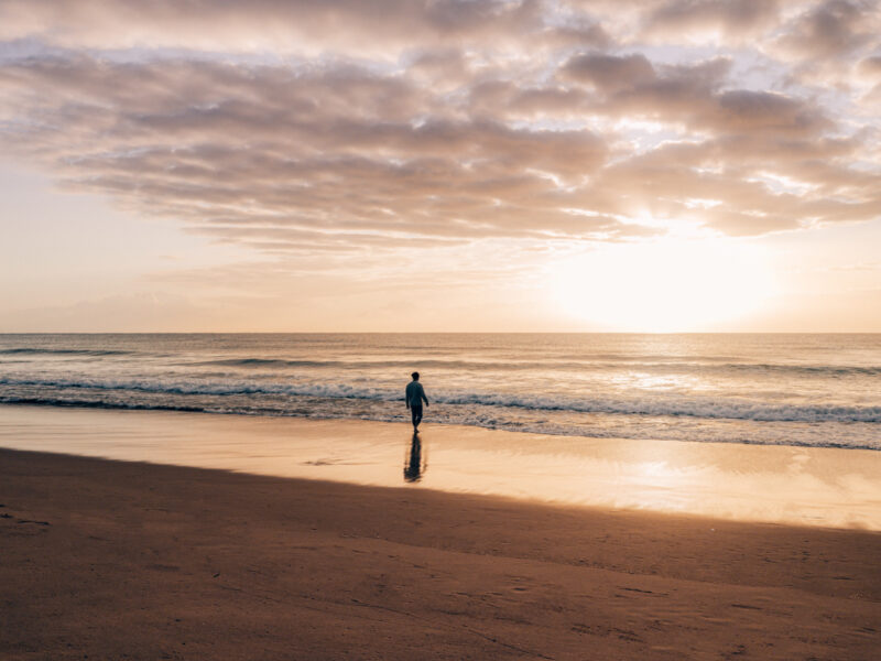 sunset beach photo with man in the distance walking towards the water