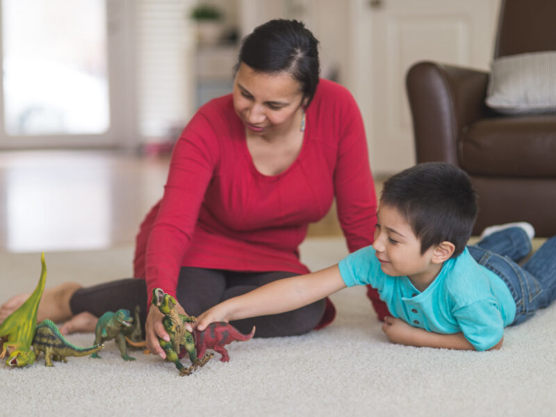 Mother playing with son and dinosaurs.