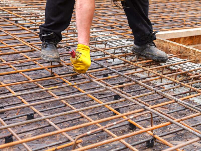 The worker ties steel reinforcing bars with wire to strengthen the foundation. Close-up. Daylight.