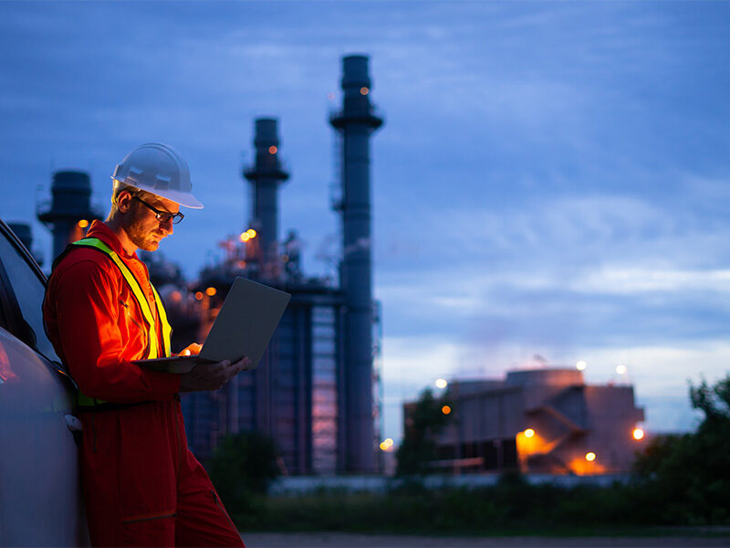 Construction worker finishing day at the plant, in the background, looking at laptop before leaving.