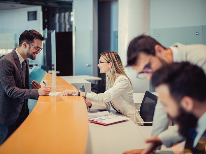 A young man is standing at a bank counter. Because of the good negotiation skills of an efficient employee, he decided to cooperate with her and sign a contract.